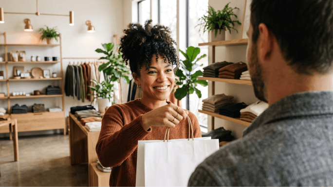 Propriétaire d’une petite entreprise remettant un sac d’achat de boutique à un acheteur lors du paiement.